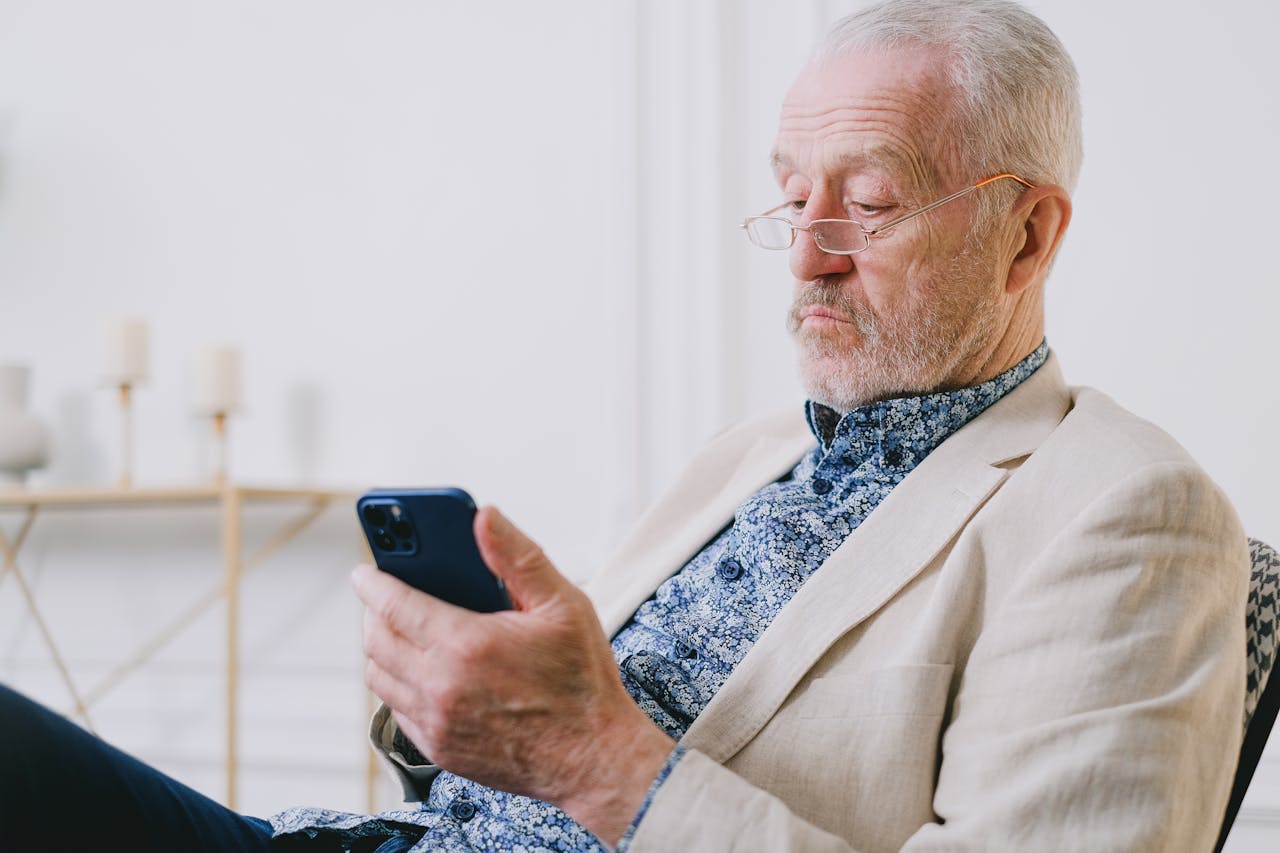 services-02 An elderly man with eyeglasses using a smartphone indoors. Close-up shot showcasing facial expression.